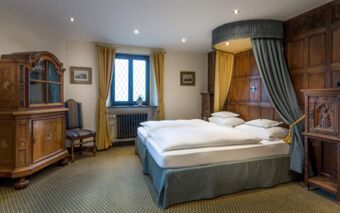 Double bed with canopy and white linens against wood-paneled wall in guest room at Burghotel Auf Sch&ouml;nburg with wooden furniture