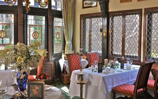 Dining area with white tablecloths, red cushioned chairs, stained glass windows, and floral arrangements in Burghotel Auf Sch&ouml;nburg