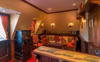Cozy sitting area with striped cushions, wooden table, an old stove, bookshelf, and red patterned curtains at Burghotel Auf Sch&ouml;nburg