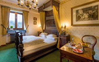 Double bed with wooden canopy and yellow drapes in a vintage room with green carpet at Burghotel Auf Sch&ouml;nburg