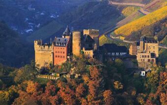 Burghotel Auf Sch&ouml;nburg castle surrounded by trees with autumn colors and vineyards on rolling hills in sunlight