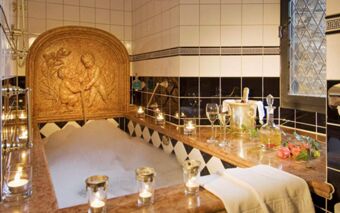 A bubble bath in a decorative marble tub with cherub fountain, lit candles, wine glasses, a champagne bucket, and flowers at Burghotel Auf Sch&ouml;nburg