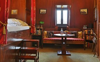 Cozy wooden interior with a red cushioned bench, small table, bed with white linens, bookshelves, and window at Burghotel Auf Sch&ouml;nburg