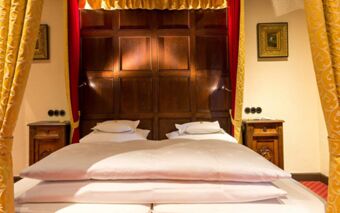 Double bed with white linens flanked by wooden bedside tables, yellow curtains, and a wooden panel headboard at Burghotel Auf Sch&ouml;nburg