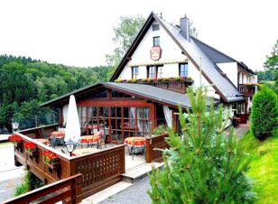Gasthof u. Pension Waldeck с открытой площадкой и террасой в идиллическом лесном и горном пейзаже, деревенской архитектурой и столами с красными скатертями.