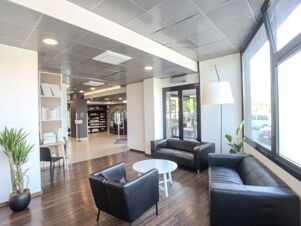 Black leather sofas and chairs with white tables on wooden floor near large windows in the B&B Hotel Firenze Novoli lobby