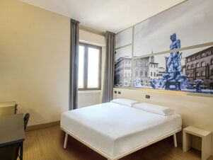Bedroom with white bed, wooden floor, window with gray curtains, and wall mural of a fountain at B&B Hotel Firenze Novoli