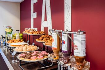 Bakery and beverage self-serve buffet with pastries, donuts, and fruit juice dispensers at B&B Hotel Firenze Novoli