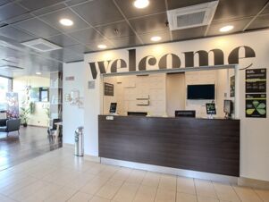 Reception desk with "welcome" sign above and informational posters visible in the lobby area of B&B Hotel Firenze Novoli
