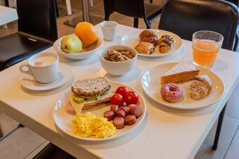 Breakfast spread with scrambled eggs, sausages, sandwich, yogurt with nuts, fruits, coffee, juice, and pastries at B&B Hotel Firenze Novoli