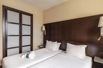 A twin bed setup with white linens, pillows, towels, wooden headboard, and sliding closet doors in B&B Hotel Arezzo room