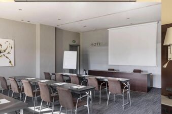 Meeting room at B&B Hotel Arezzo with chairs, tables, projector screen, whiteboard, and abstract wall art visible