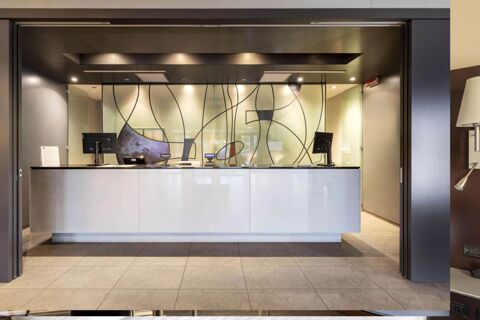 Reception desk with two computer monitors, modern lighting, and decorative glass partition at B&B Hotel Arezzo