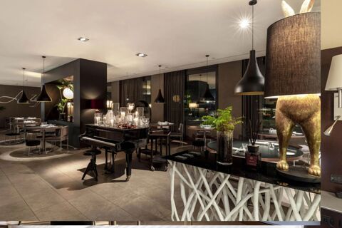 Modern dining area of B&B Hotel Arezzo featuring a black grand piano with candles, pendant lights, tables, and chairs in neutral tones