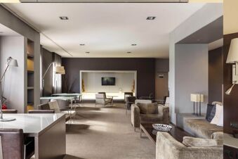 Spacious lounge area at B&B Hotel Arezzo with armchairs, sofas, tables, floor lamps, and a wall-mounted TV in a modern setting