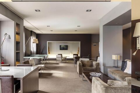 Spacious lounge area at B&B Hotel Arezzo with armchairs, sofas, tables, floor lamps, and a wall-mounted TV in a modern setting