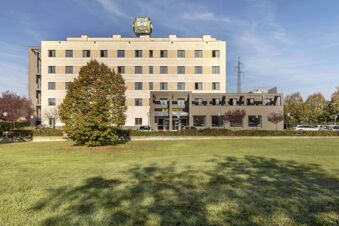 A five-story beige building with multiple windows, a large green tree in front, cars parked, and B&B Hotel Arezzo signage visible on top and entrance