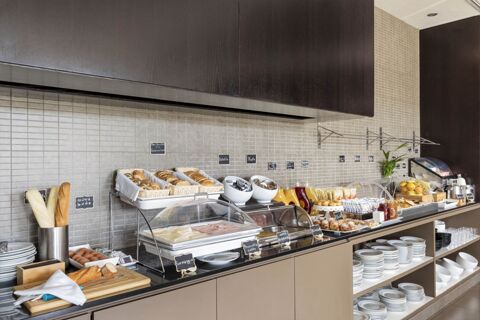 Breakfast buffet with bread, pastries, juices, condiments, plates, and cups at B&B Hotel Arezzo breakfast area