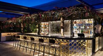 Outdoor bar area at Anantara Palazzo Naiadi Rome Hotel with illuminated counter, bar stools, floral decorations, and liquor bottles displayed
