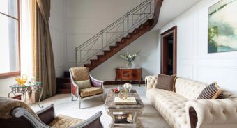 Living room with cream tufted sofa, two armchairs, marble coffee table, wooden staircase, and decor at Anantara Palazzo Naiadi Rome Anantara Palazz