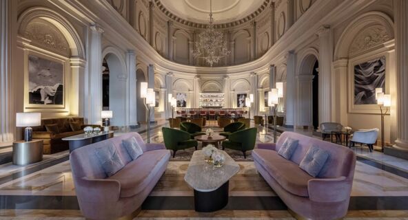 Spacious lounge at Anantara Palazzo Naiadi Rome Hotel with curved walls, chandeliers, sofas, green chairs, and a marble floor
