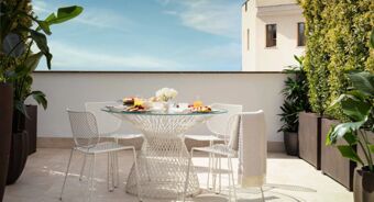 Outdoor terrace with a glass-top table set for breakfast and surrounded by white chairs and plants at Anantara Palazzo Naiadi Rome
