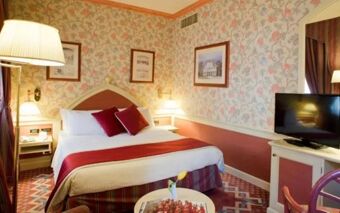 Hotel Regency Milano guest room with a large bed, floral wallpaper, bedside lamps, framed pictures, and a TV on a white cabinet
