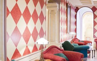 Red and cream diamond patterned wall with red and green upholstered armchairs and a lamp at Hotel Regency Milano