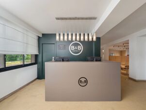 Reception area with two Lenovo computer monitors, hanging cylindrical lights, and B&B Hotel Padova Methis logo on wall and desk