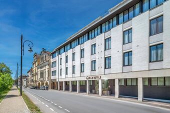 Modern white building with many large windows and street lamps along the road near B&B Hotel Padova Methis under a clear blue sky