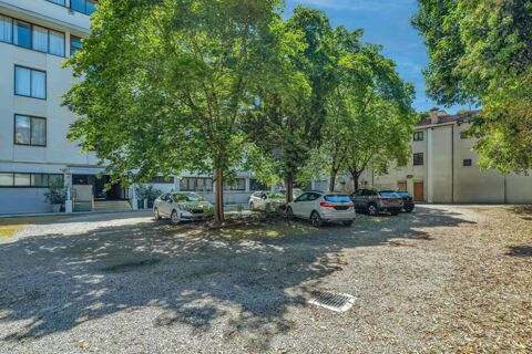 Parking area with several cars under large leafy green trees beside a white building and smaller structure at B&B Hotel Padova Methis
