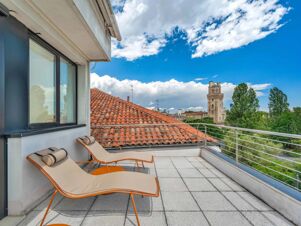 Two beige lounge chairs with cylindrical pillows on a rooftop terrace with a red tile roof and a tall tower in the distance at B&B Hotel Padova Methis