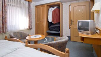 Hotel room at Gasthof Zur Linde showing two beds, a round table with two chairs, an open wooden wardrobe, and a TV on a wall shelf