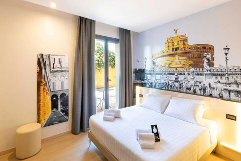 Modern hotel room with a large bed, two folded towels, wall art of a historic building, and a glass door at B&B Hotel Roma Tuscolana San Giovanni