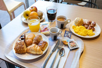 Breakfast tray with various pastries, scrambled eggs, sausages, fruit, and drinks served at B&B Hotel Roma Tuscolana San Giovanni