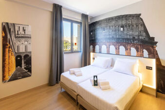 Two single beds with white linens and towels in a hotel room at B&B Hotel Roma Tuscolana San Giovanni with Colosseum wall art