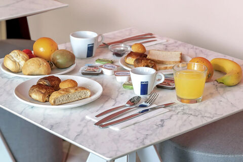 A breakfast spread on a marble table with fruit, pastries, bread, two white Lavazza coffee cups, and a glass of orange juice at B&B Hotel Roma Tuscolana San Giovanni