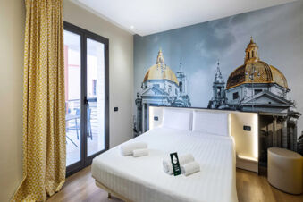 Modern hotel room at B&B Hotel Roma Tuscolana San Giovanni with a large bed, wall mural of domed buildings, and balcony door