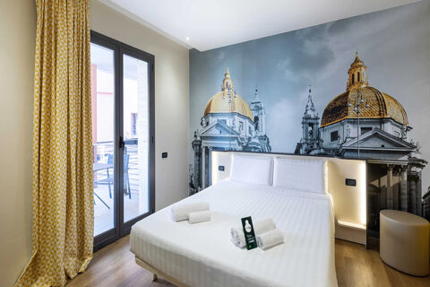 Modern hotel room at B&B Hotel Roma Tuscolana San Giovanni with a large bed, wall mural of domed buildings, and balcony door