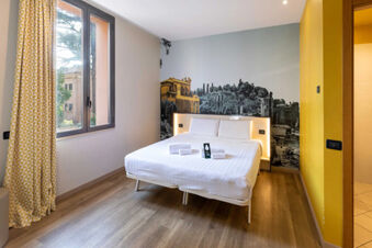 Guest room at B&B Hotel Roma Tuscolana San Giovanni with a double bed, white linens, a cityscape wall mural, and yellow curtains