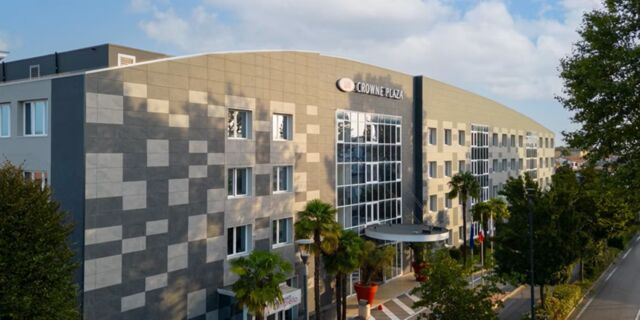 Modern multi-story building with grey and beige tiled exterior and large glass windows at Crowne Plaza Venice East hotel