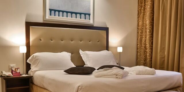 Double bed with white linens and brown pillows, beige tufted headboard, two nightstands with lamps at Crowne Plaza Venice East