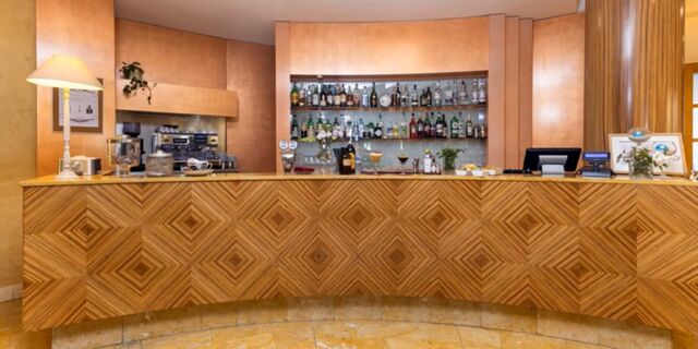 Reception desk with geometric wood paneling, a lamp, coffee machine, and assorted bottles behind at Crowne Plaza Venice East