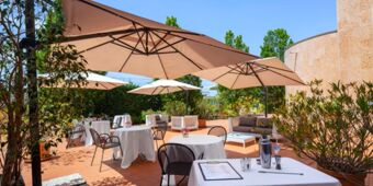 Outdoor patio dining area at Crowne Plaza Venice East with tables covered in white cloth and large beige umbrellas
