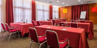 Conference room at Crowne Plaza Venice East with red tablecloths and chairs, water bottles, glasses, and notepads on tables