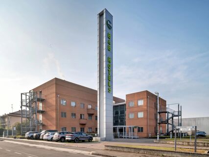 Tall vertical sign with B&B Hotel logo and text stands in front of the brown building with parked cars at B&B Hotel Milano Cologno Studios