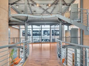 Interior view of a modern space with curved metal railings, wooden floor, brick walls, and black and white photos in B&B Hotel Milano Cologno Studios