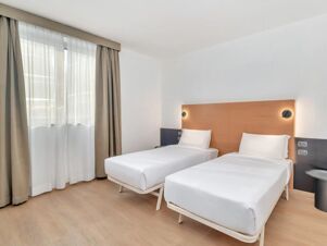 Two single beds with white linens next to a window with beige curtains in a room at B&B Hotel Milano Cologno Studios