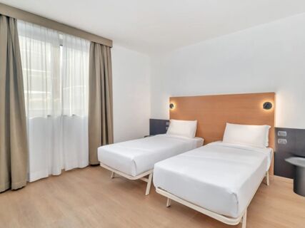 Two single beds with white linens next to a window with beige curtains in a room at B&B Hotel Milano Cologno Studios