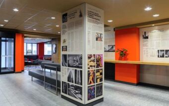 Interior of Hotel ibis Milano Centro showing informational panels on columns, modern seating area, and red-orange accents